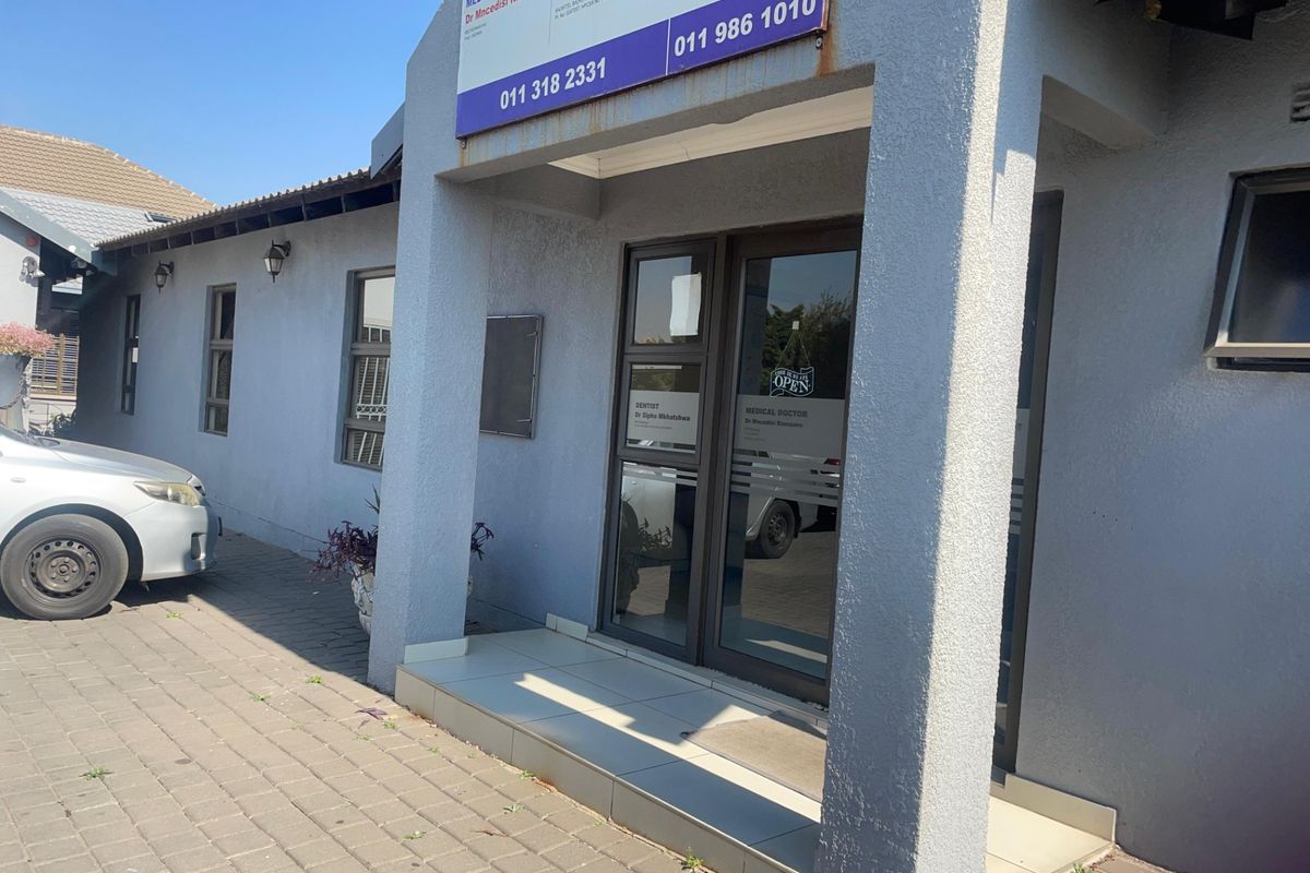 Front entrance of a commercial property featuring a paved driveway, aluminium glass door, and exterior signage.