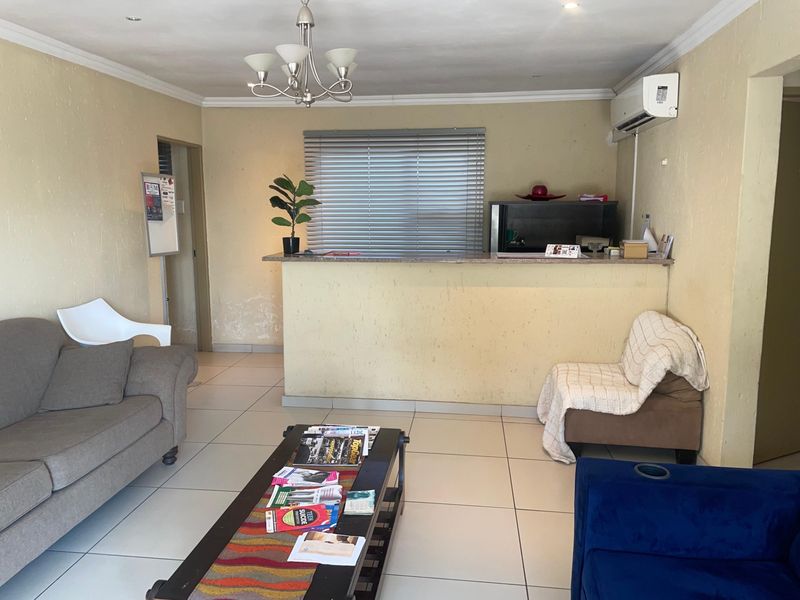 Open plan living area featuring tiled flooring, a breakfast bar, and wall-mounted air conditioning unit, showing signs of wear on the lower wall sections.