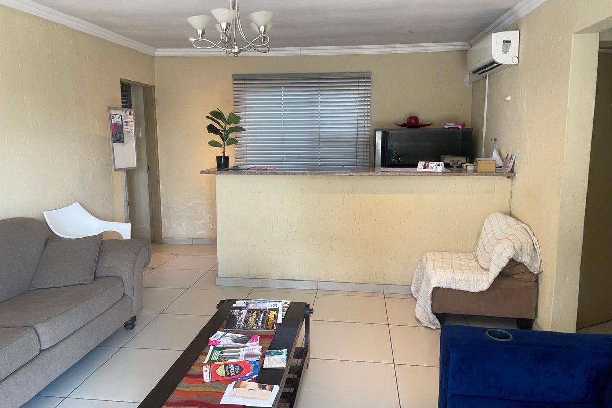 Open plan living area featuring tiled flooring, a breakfast bar, and wall-mounted air conditioning unit, showing signs of wear on the lower wall sections.