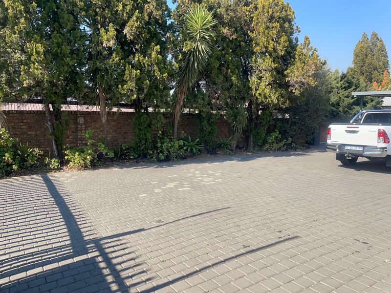 A paved driveway area featuring a brick boundary wall and established perimeter trees, providing secure off-street parking space.