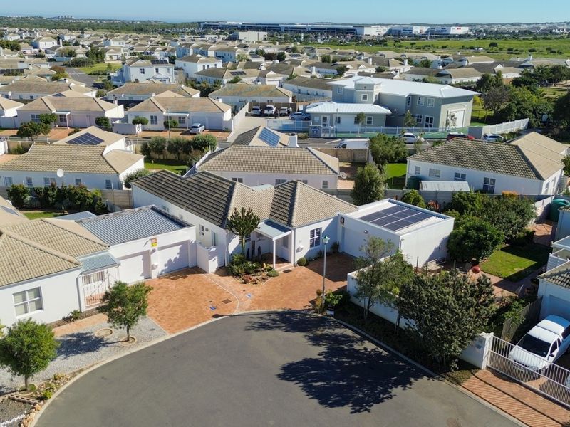 Aerial view of a residential property featuring a paved driveway, multiple garages, and solar panels installed on the tiled roof within a suburban estate.
