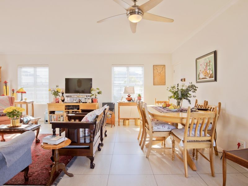 Spacious open-plan living and dining area featuring neutral tiled flooring, a central ceiling fan, and large windows with venetian blinds.