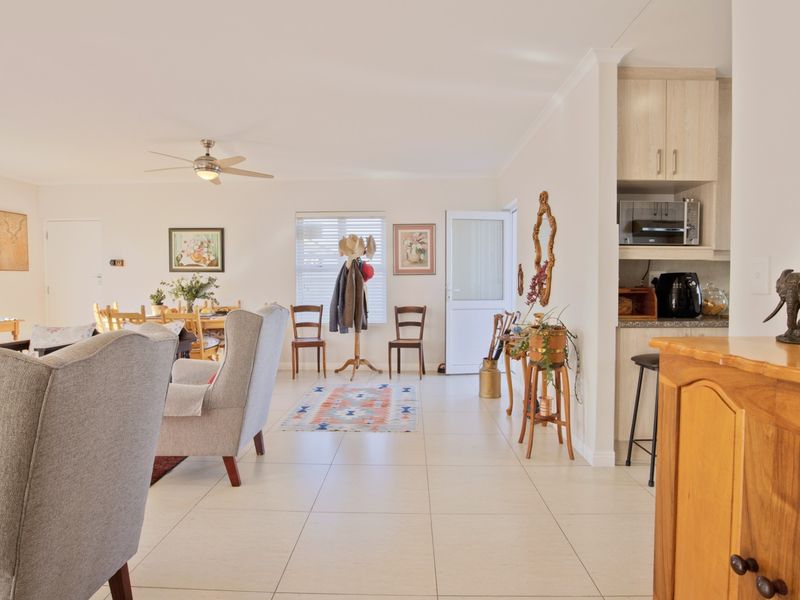 Spacious open-plan living area featuring neutral tiled flooring, a ceiling fan, and a compact kitchen nook with built-in cabinetry and stone countertops.