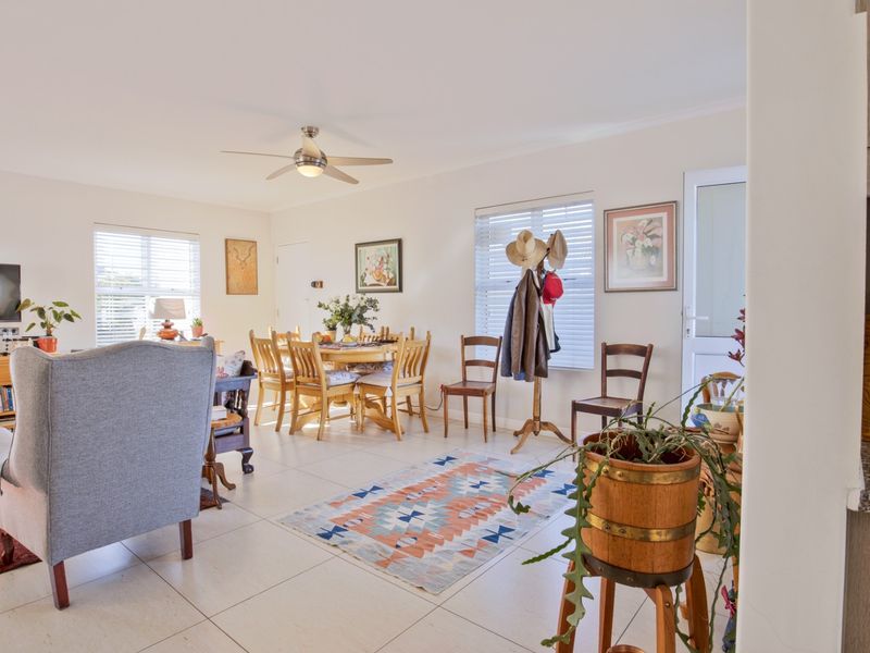 A bright open-plan living and dining area featuring neutral tiled flooring, a ceiling fan, and large windows with venetian blinds.