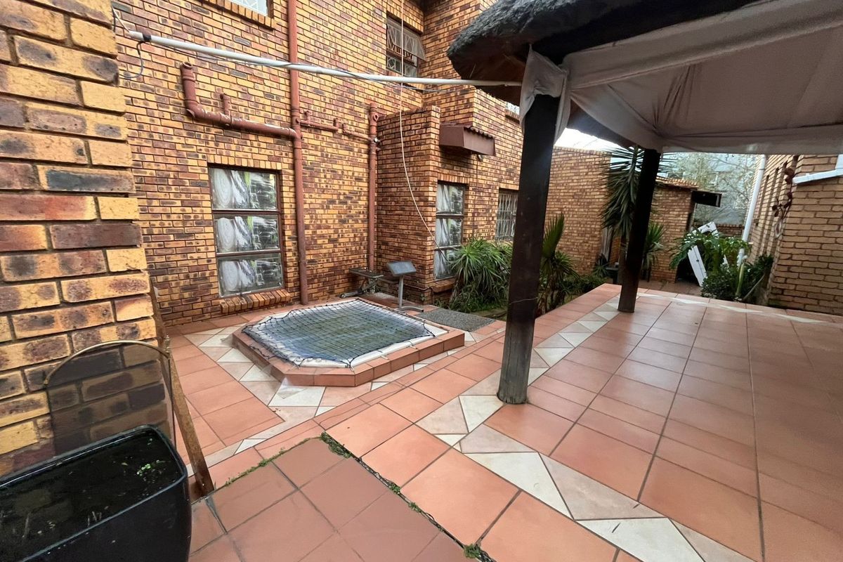 Rear exterior area featuring a tiled patio, a thatched lapa, and a sunken water feature against a face-brick building facade.