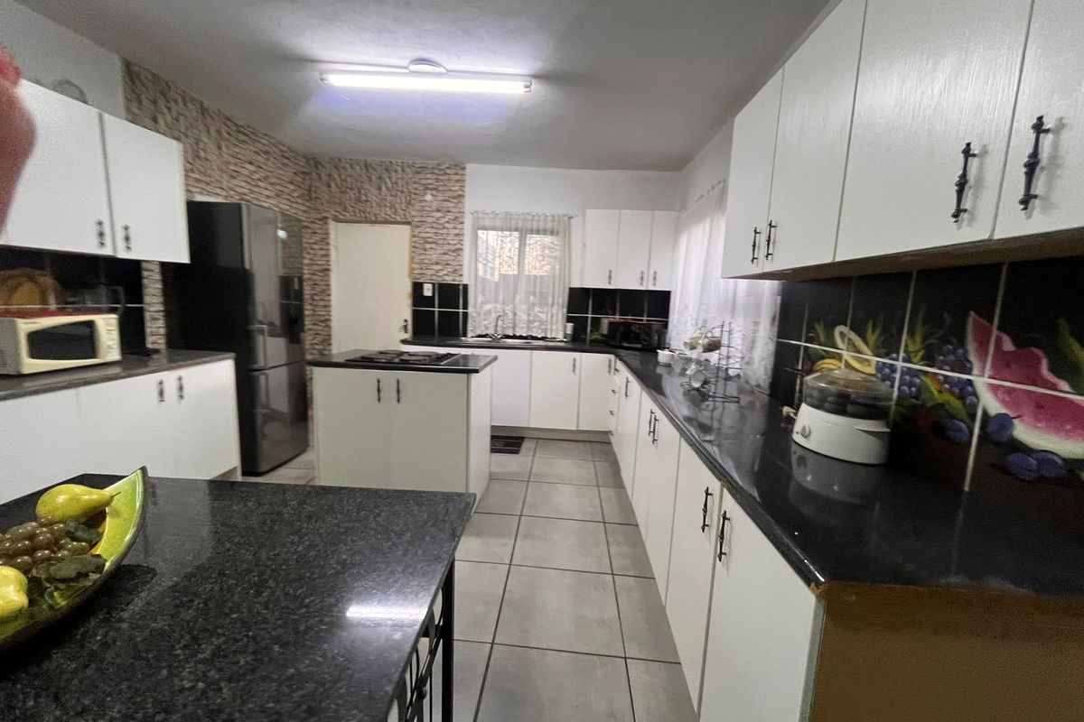Spacious kitchen featuring white cabinetry, dark granite countertops, a central island with a cooktop, and ceramic tile flooring.