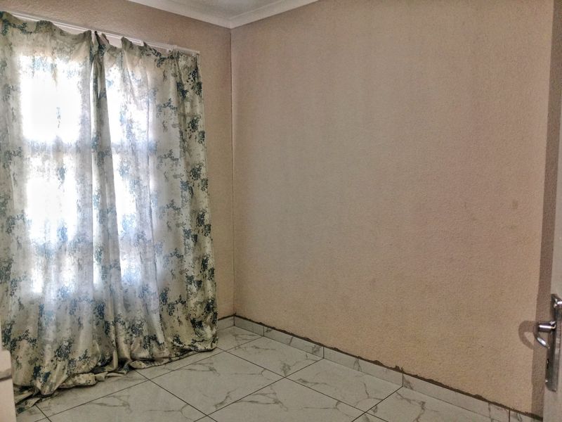 An empty bedroom featuring tiled flooring and a window, requiring minor cosmetic updates to the walls and skirting.