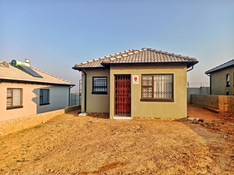 Front view of a single-story residential house featuring a tiled roof, security gate, and burglar bars, set on an unlandscaped plot.