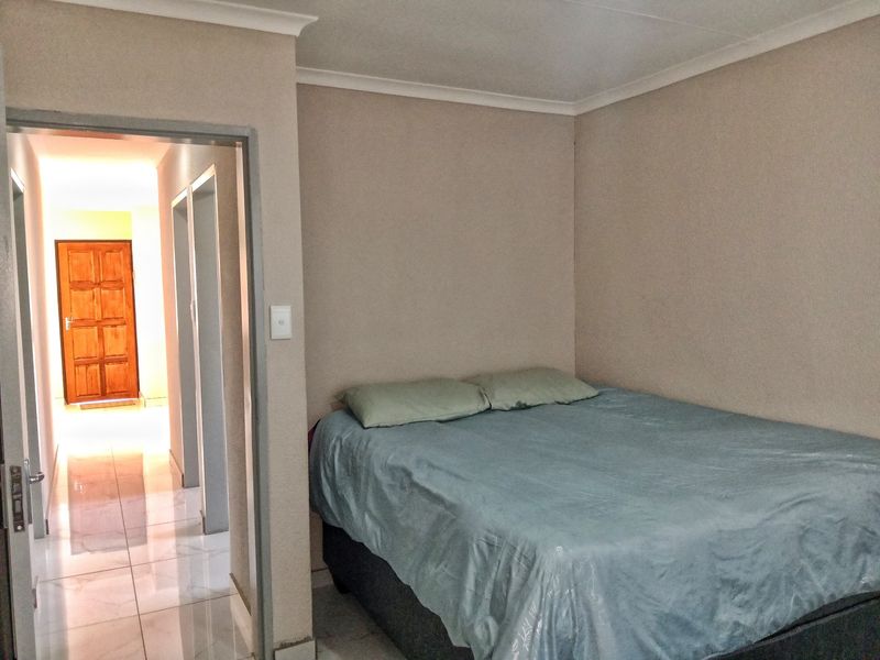 A bedroom featuring neutral wall tones, cove cornicing, and tiled flooring, with an adjacent hallway leading to a wooden door.