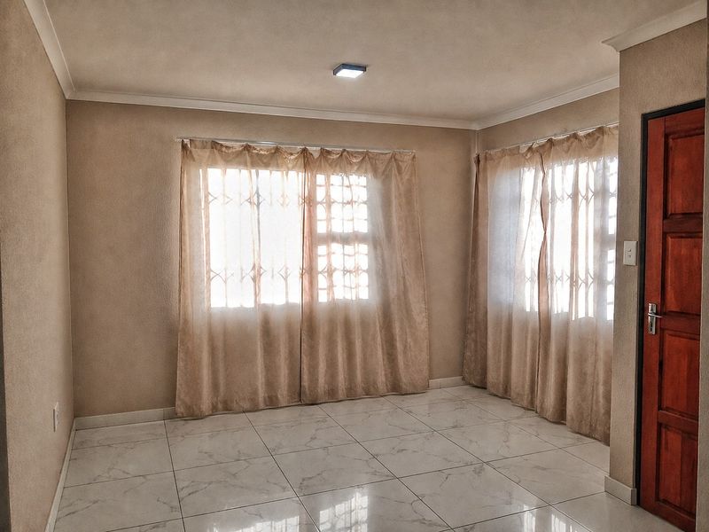 A bright, empty living room featuring neutral walls, white marble-look tiled flooring, and security gates on the windows.