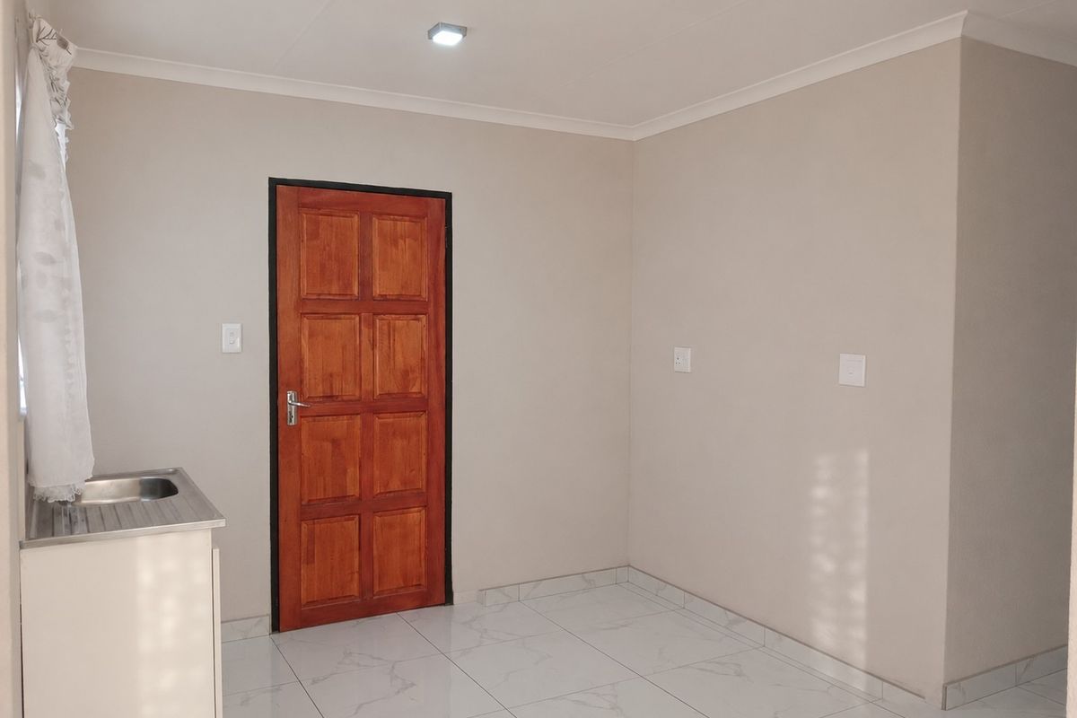 A clean, minimalist kitchen area featuring modern white marble-look floor tiles, a stainless steel sink unit, and a solid timber door.