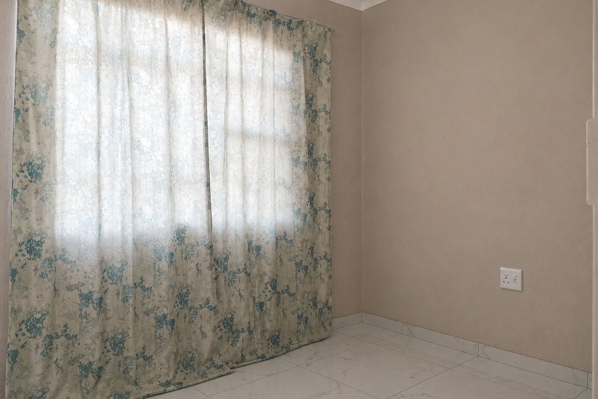 A clean, empty bedroom featuring neutral wall tones, tiled flooring, and a large window with curtains, providing a versatile space ready for personalization.