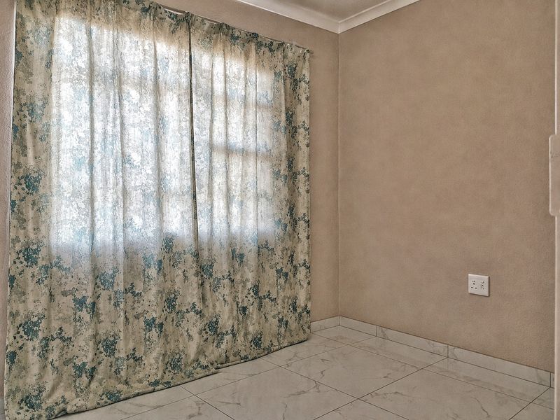 An empty bedroom featuring neutral wall finishes, tiled flooring, and a window dressed with floral curtains.
