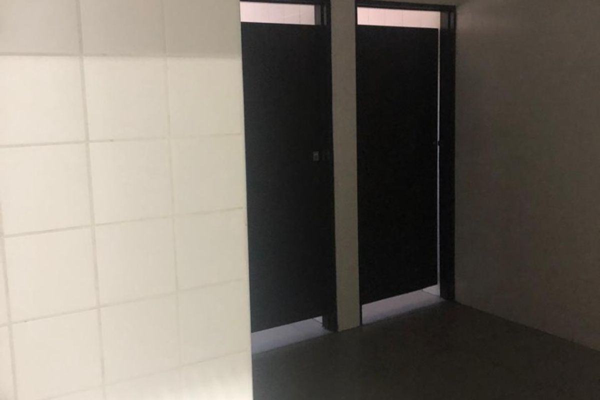 A functional bathroom space featuring tiled flooring, a tiled partition wall, and two doorways leading to private stalls.