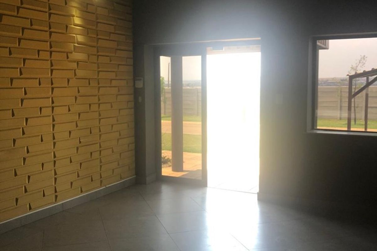 Spacious living area featuring a textured feature wall, tiled flooring, and modern lighting, with direct access to the exterior through a sliding glass door.