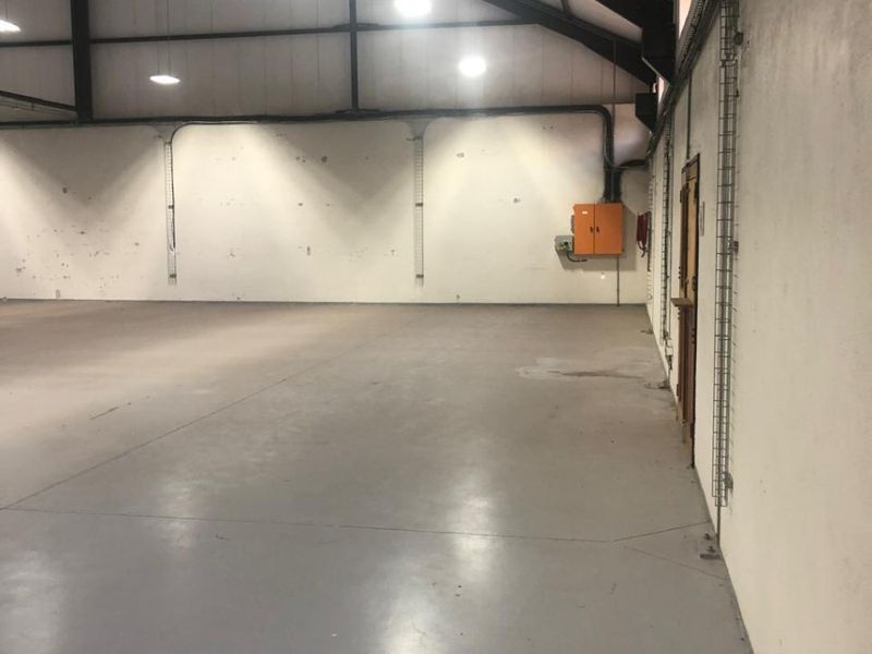 Spacious industrial warehouse unit featuring high ceilings with exposed steel trusses, polished concrete flooring, and functional surface-mounted electrical infrastructure.