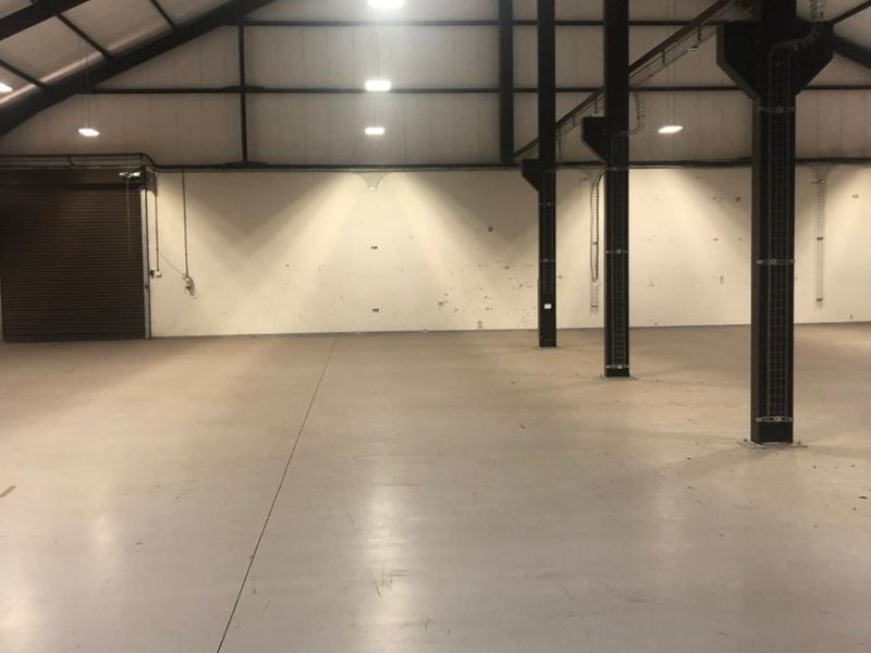 Spacious industrial warehouse unit featuring high ceilings, exposed steel structural columns, durable concrete flooring, and a large roller shutter door for easy access.