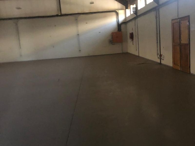 Spacious industrial warehouse unit featuring high ceilings with exposed steel trusses, concrete flooring, and functional fire safety equipment.