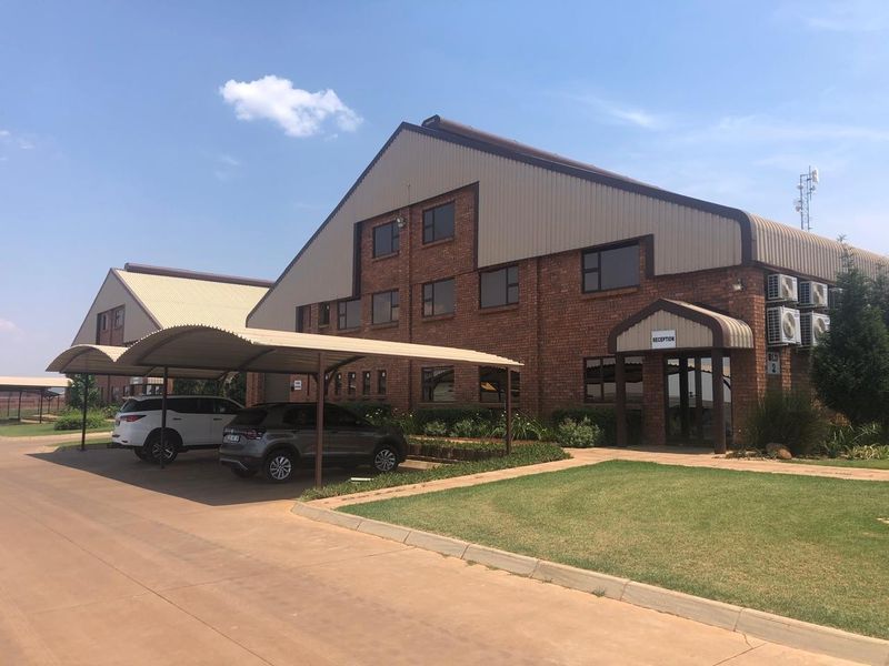 Exterior view of a multi-story industrial brick building featuring a reception entrance, metal roofing, and covered parking bays.