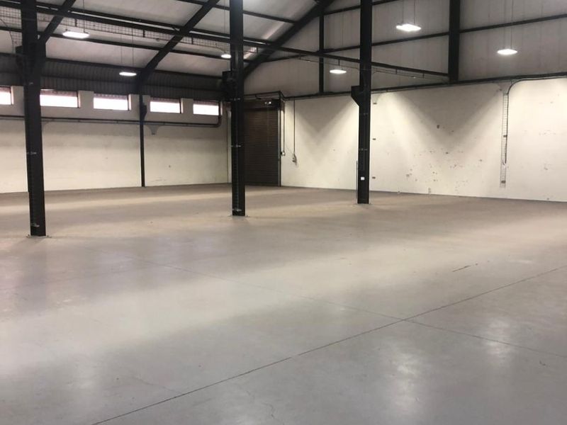 Spacious industrial warehouse featuring a high-pitched steel portal frame, polished concrete flooring, and functional industrial lighting throughout the open-plan area.