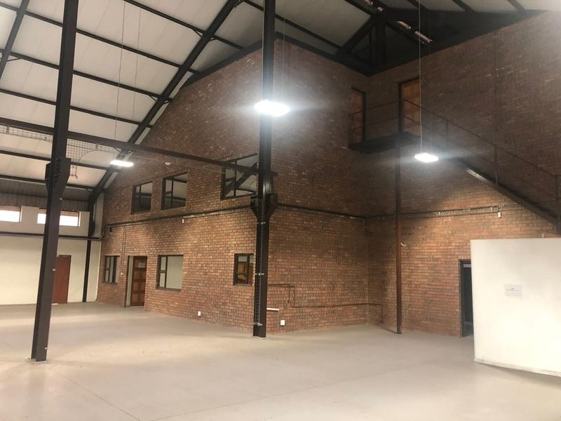 Spacious industrial warehouse unit featuring exposed brick walls, high ceilings with steel trusses, concrete flooring, and a mezzanine level with staircase access.