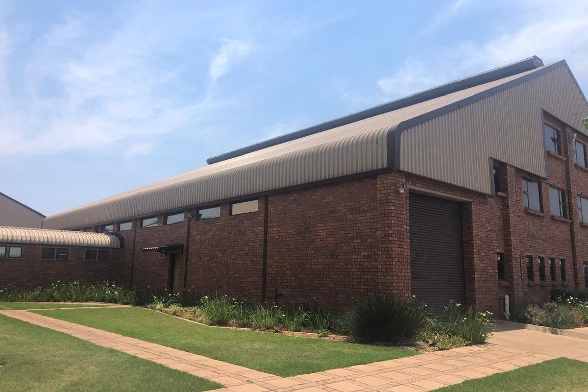 Exterior view of an industrial building featuring a brick facade, metal roofing, a large roller shutter door, and well-maintained surrounding paved walkways and gardens.