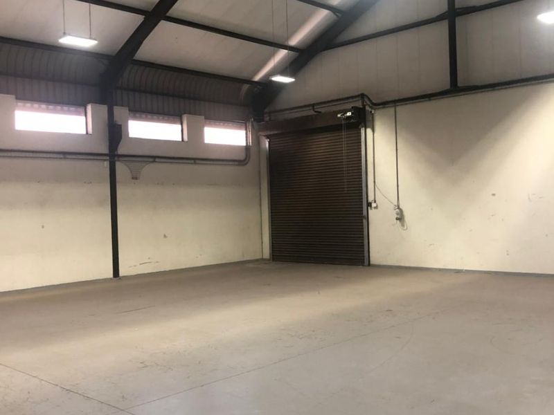 Spacious industrial warehouse unit featuring high ceilings, exposed steel portal frame, concrete flooring, and a large roller shutter door for easy access.
