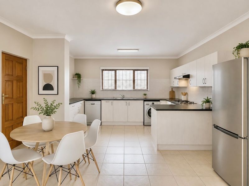 A bright open-plan kitchen and dining area featuring modern white cabinetry, dark countertops, tiled flooring, and integrated appliances in a well-maintained space.