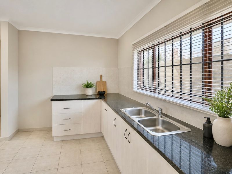 A clean and functional kitchen featuring light-toned cabinetry, dark granite countertops, a double stainless steel sink, and tiled splashbacks with natural light.