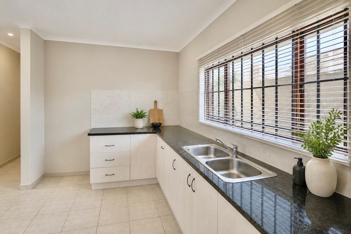 A clean and functional kitchen featuring light-toned cabinetry, dark granite countertops, a double stainless steel sink, and tiled splashbacks with natural light.