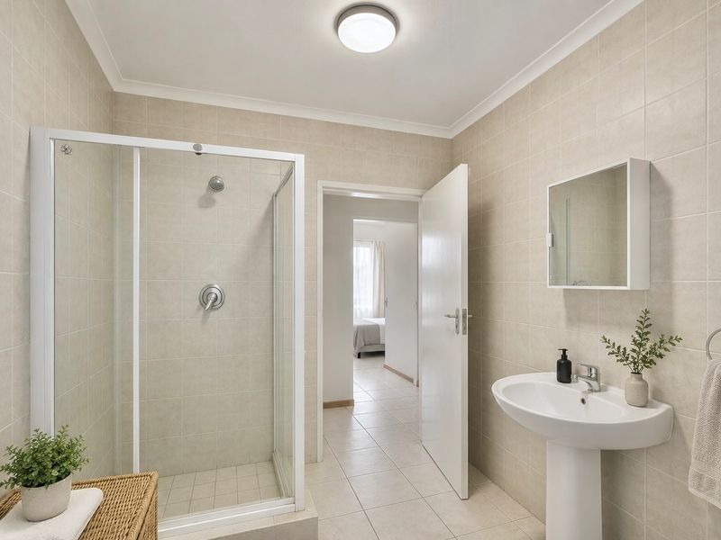 A clean, neutral-toned bathroom featuring a glass-enclosed shower, pedestal basin, and wall-mounted medicine cabinet, offering a functional and well-maintained space.