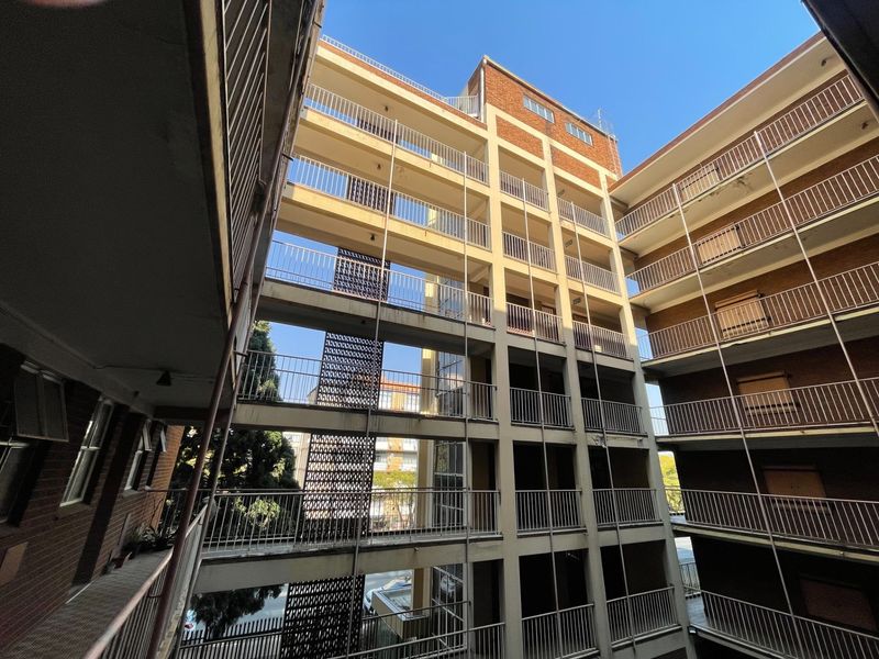 View of the apartment building's exterior courtyard featuring multi-level concrete walkways, metal railings, and a decorative breeze block screen.