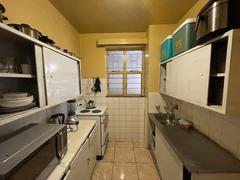 A compact, functional kitchen featuring built-in cabinetry, a stainless steel sink, tiled backsplash, and a freestanding stove with security bars on the window.