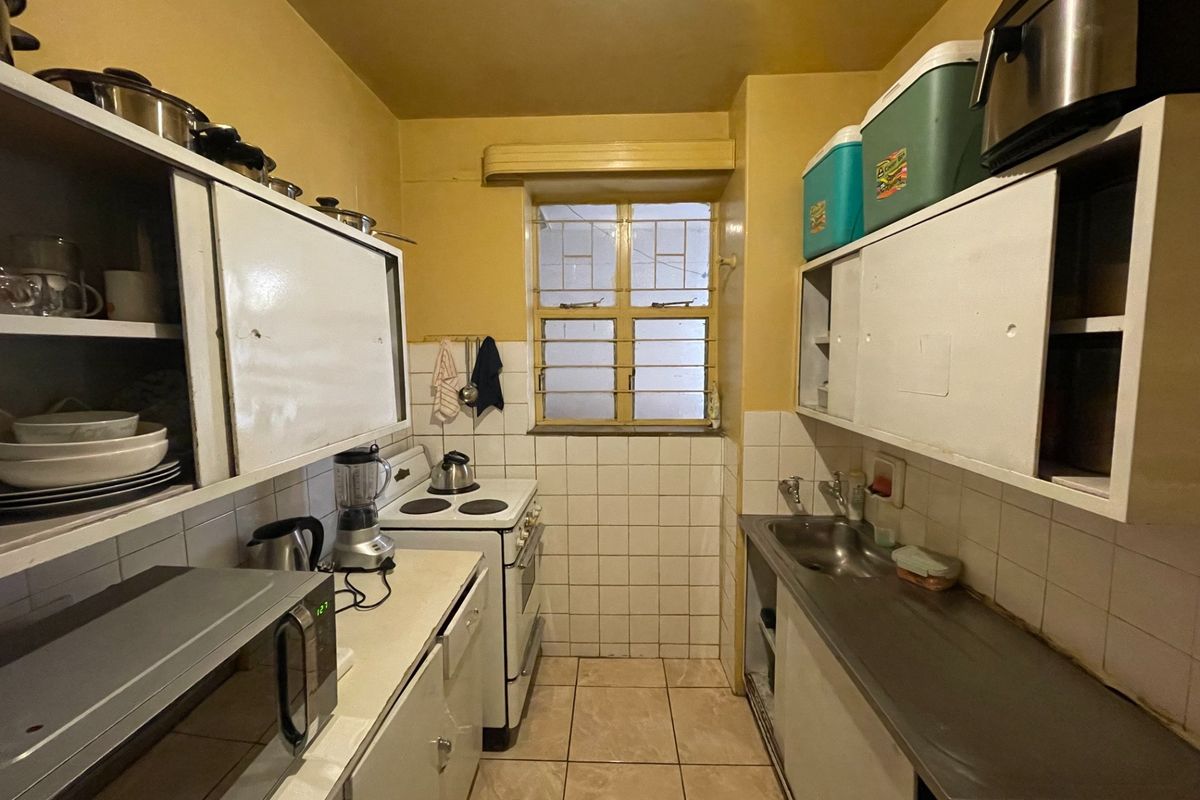 A compact, functional kitchen featuring built-in cabinetry, a stainless steel sink, tiled backsplash, and a freestanding stove with security bars on the window.