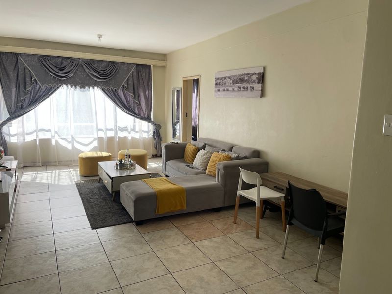 A spacious living room featuring tiled flooring and a large window, offering a bright and functional area for relaxation.