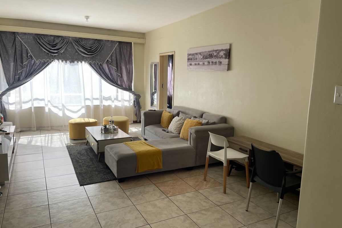 A spacious living room featuring tiled flooring and a large window, offering a bright and functional area for relaxation.