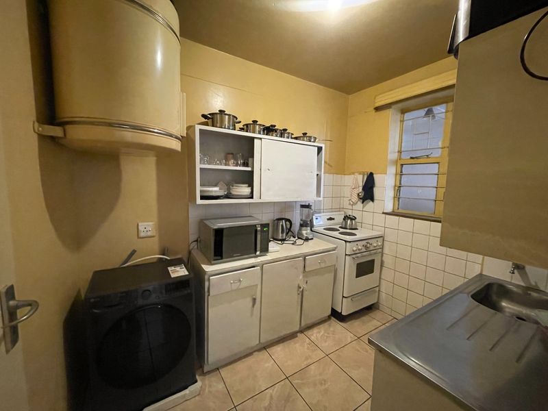 A compact, dated kitchen featuring tiled flooring, a stainless steel sink, built-in cabinetry, and a freestanding stove, offering potential for modernization.