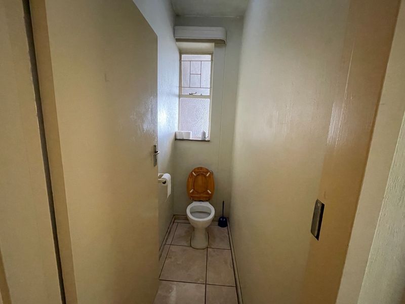 A compact, functional bathroom featuring tiled flooring and a window with security bars, presenting an opportunity for cosmetic updates.