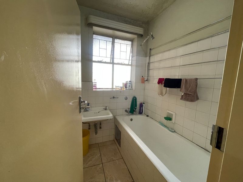 A dated bathroom featuring a bathtub, wall-mounted basin, and tiled finishes, requiring cosmetic updates to improve its overall condition and appeal.