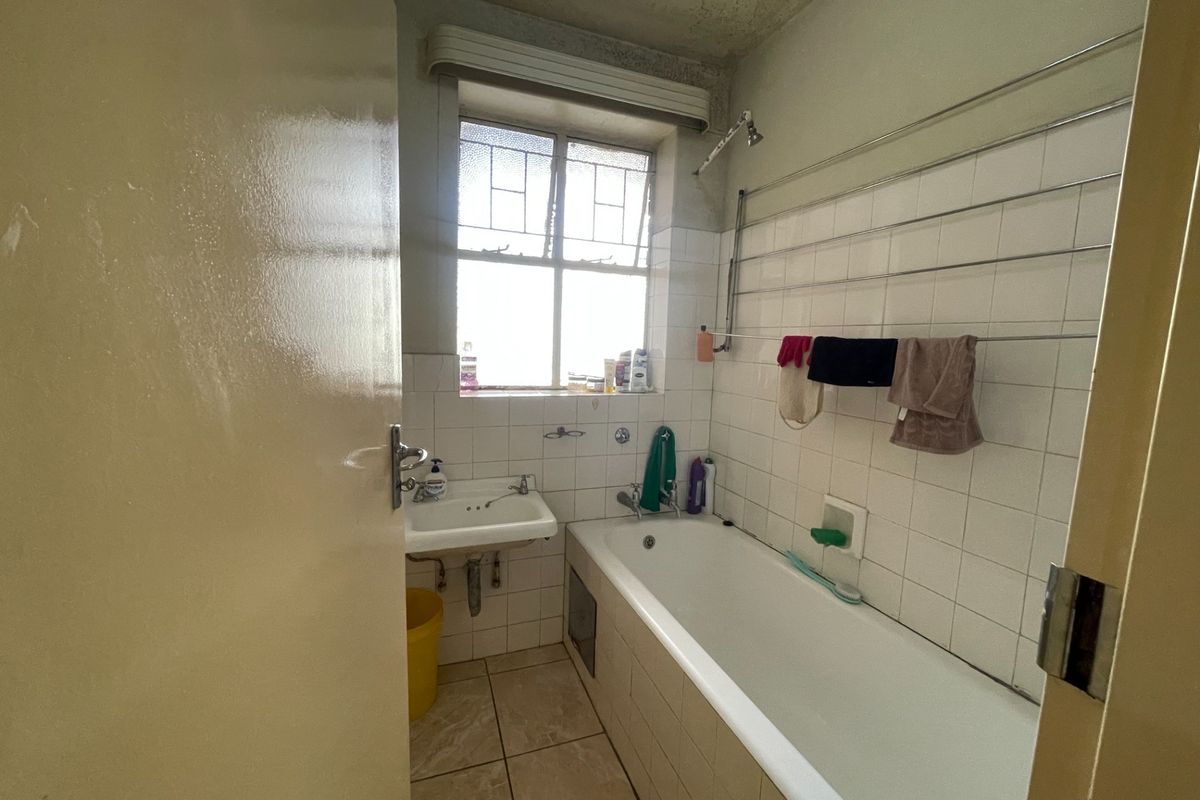 A dated bathroom featuring a bathtub, wall-mounted basin, and tiled finishes, requiring cosmetic updates to improve its overall condition and appeal.