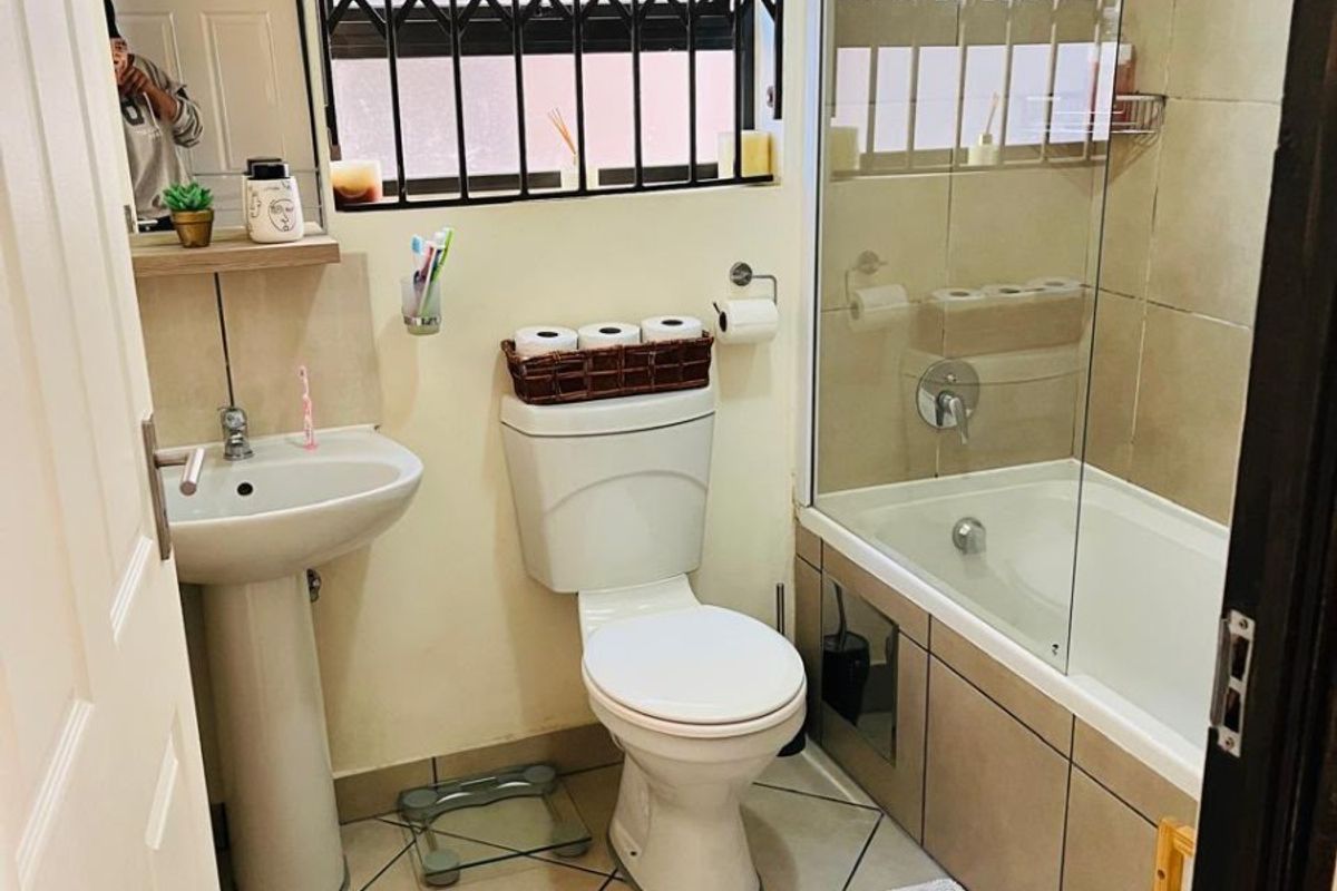A functional bathroom featuring a pedestal basin, toilet, and a bathtub with a glass shower screen and tiled finishes.