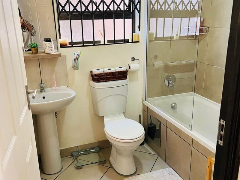 A functional bathroom featuring a pedestal basin, toilet, and a bathtub with a glass shower screen and tiled finishes.