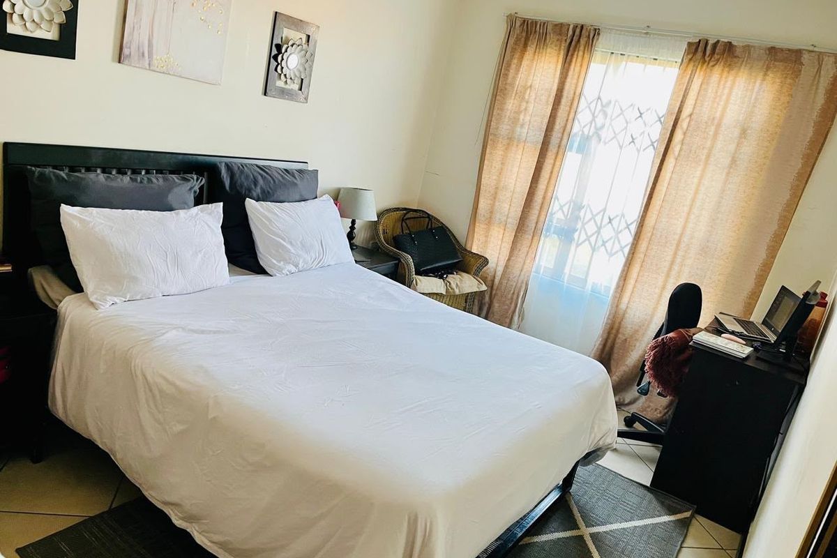 A functional bedroom featuring tiled flooring and a window fitted with a security gate, providing natural light and essential security.