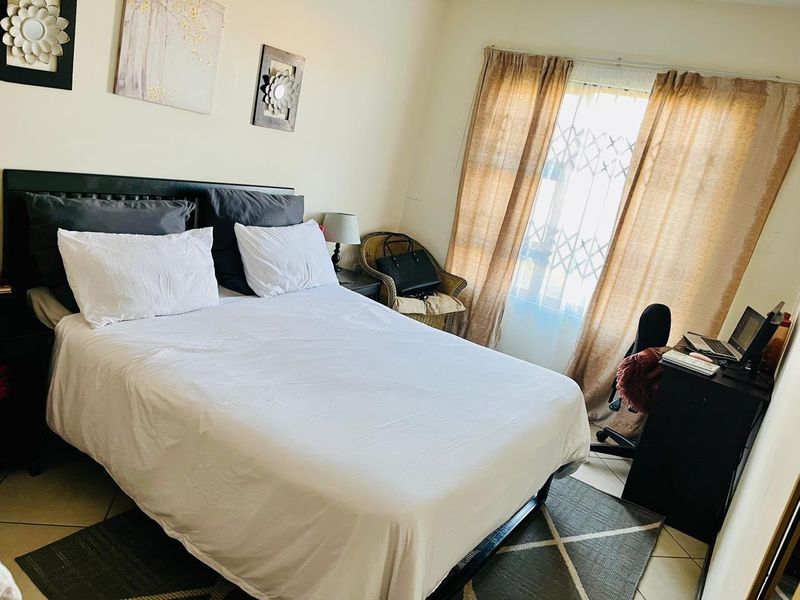 A functional bedroom featuring tiled flooring and a window fitted with a security gate, providing natural light and essential security.