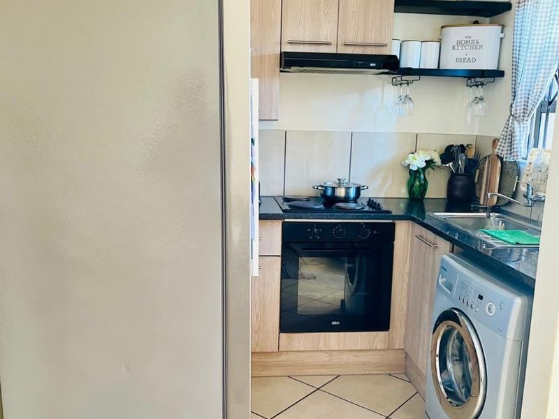 Compact kitchen featuring light wood-finish cabinetry, dark countertops, built-in oven and hob, and tiled flooring with integrated laundry plumbing.