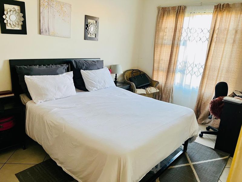A functional bedroom featuring tiled flooring and a window fitted with a security gate, providing natural light and basic security.