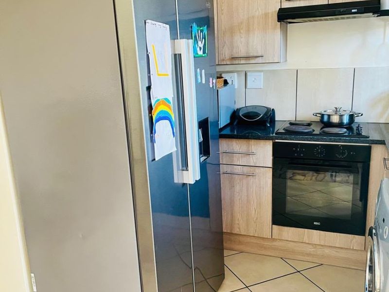 Compact kitchen featuring light wood-finish cabinetry, built-in oven, electric hob, extractor fan, and tiled flooring.