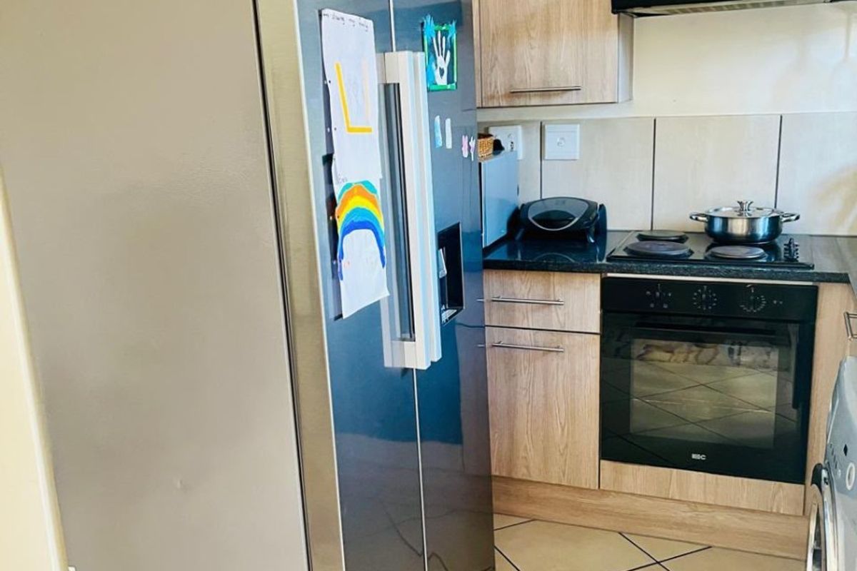 Compact kitchen featuring light wood-finish cabinetry, built-in oven, electric hob, extractor fan, and tiled flooring.