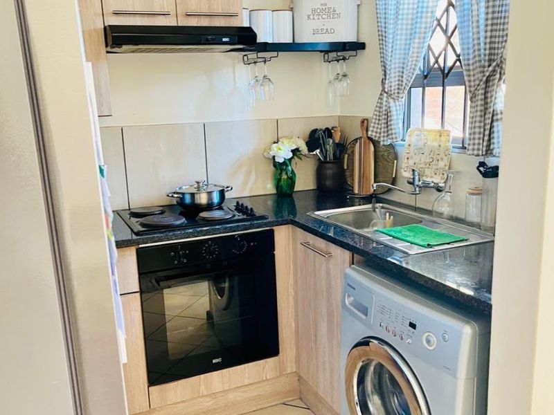 Compact and functional scullery featuring laminate cabinetry, granite countertops, built-in oven, electric hob, and integrated laundry appliance space.