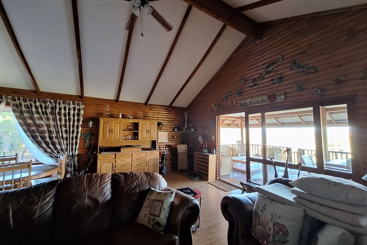 Spacious living room featuring vaulted timber ceilings with exposed beams, log-style wall cladding, and large sliding doors opening onto a covered patio.